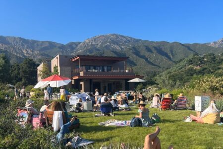 A large group of people laying on the lawn in front of the Pritzlaff Building with the Santa Ynez Mountains in the background.