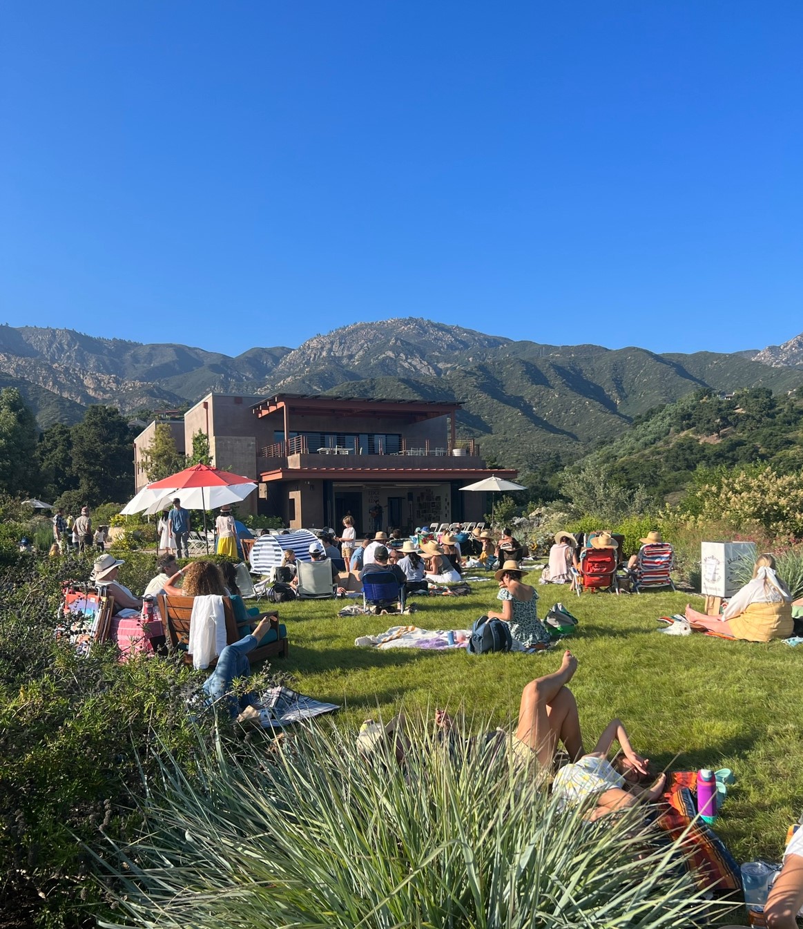 A large group of people laying on the lawn in front of the Pritzlaff Building with the Santa Ynez Mountains in the background.