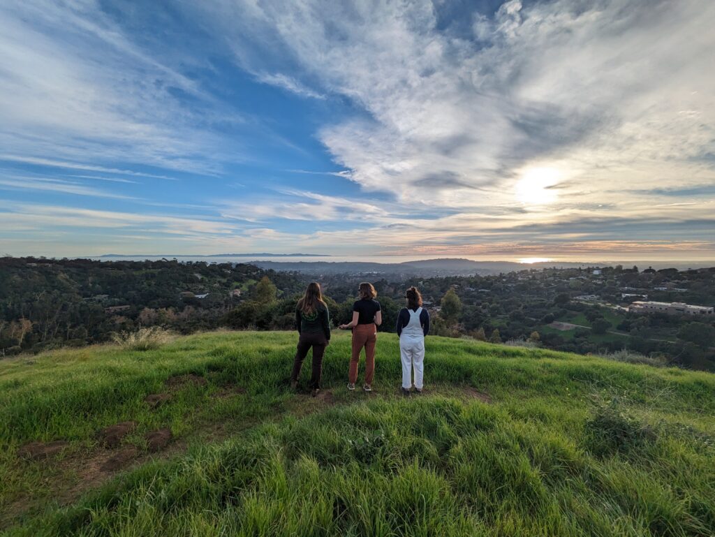 Three people looking west to the ocean and islands from the grassy meadow with a beautiful sunset.
