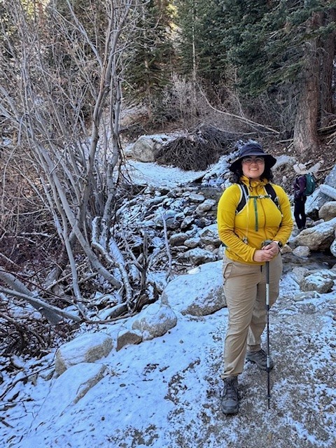 Latino woman in yellow shirt pausing for picture in snowing forest while hiking