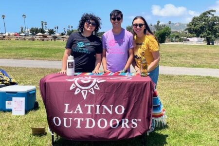 Three Latino outdoor leaders at table in park at outdoor event