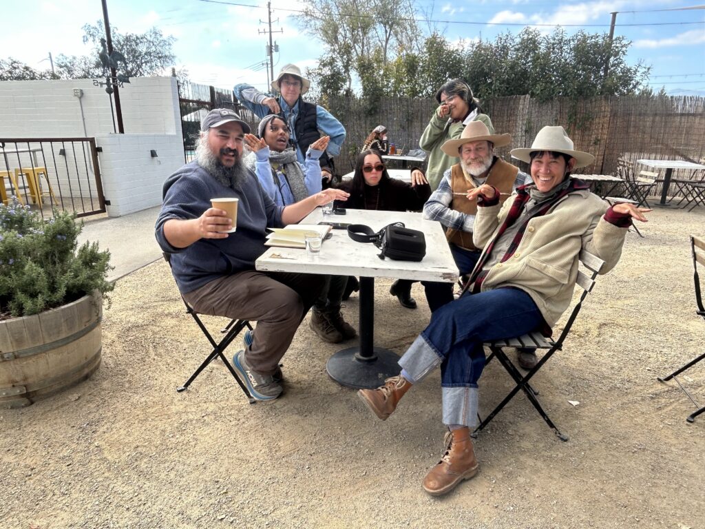 A group of birders sitting at a table doing their impressions of birds--holding arms out like wings.