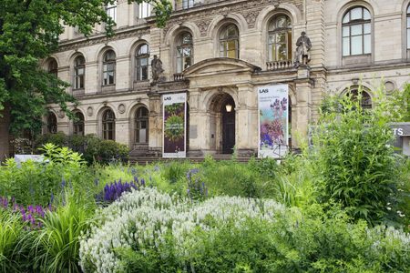 Historic building facade with lush garden and colorful flowers.